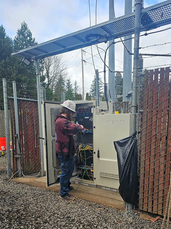 An electrician working in an electrical panel below a cell tower.