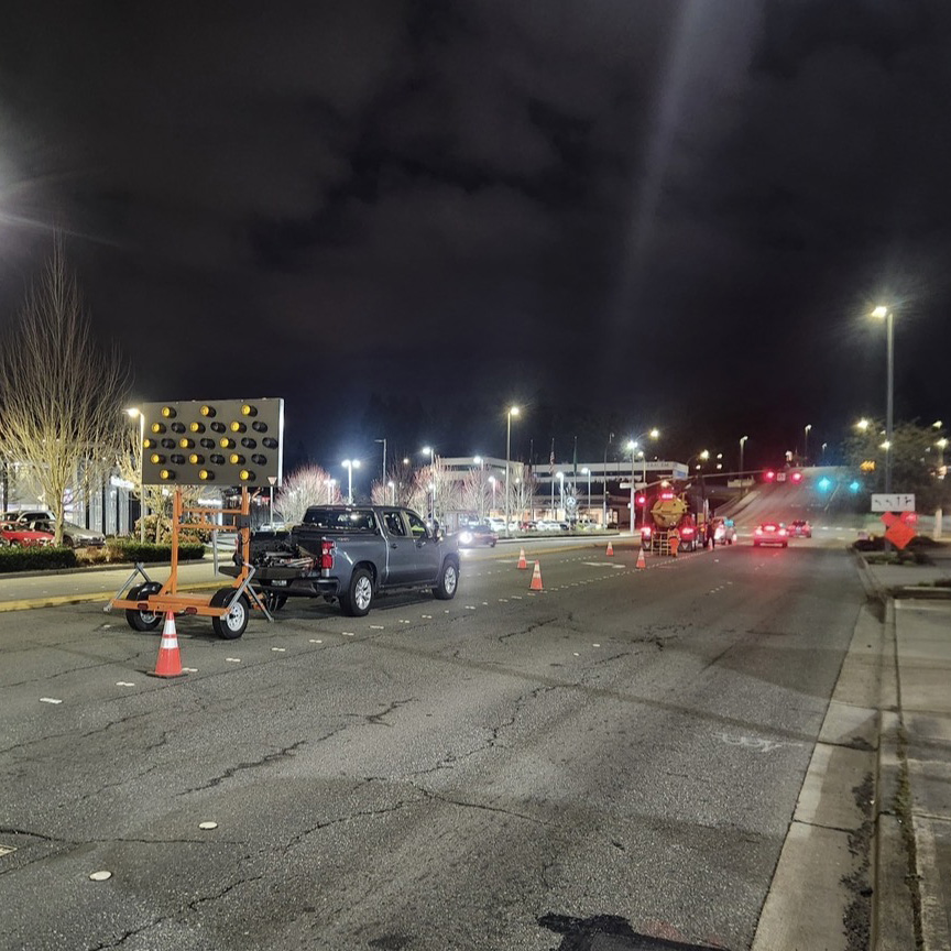 Traffic control signage and cones on a road at night.