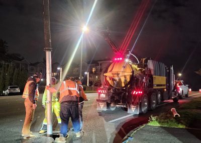 Large truck with a vacuum hose inserted in a manhole with workers around it.